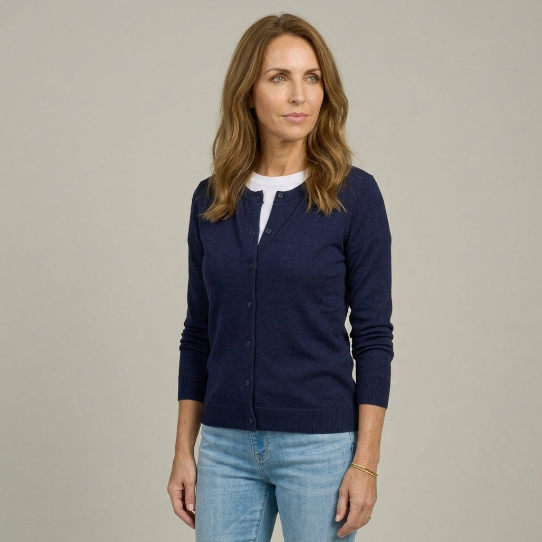 Woman wearing MagnaReady navy magnetic knit cardigan over a white shirt with light blue jeans on a beige background.
