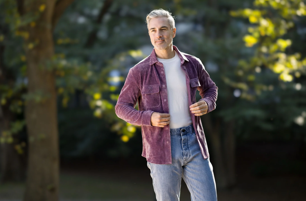 Man wearing a purple adaptive corduroy shirt with magnetic buttons, standing outdoors with trees in the background.