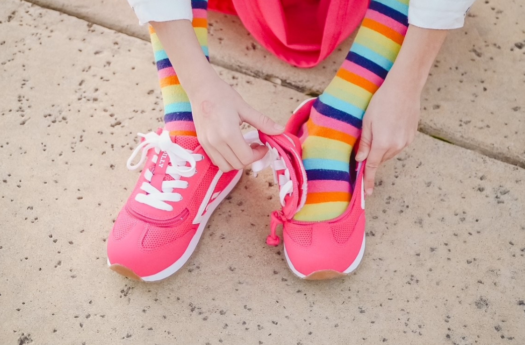 Person wearing pink adaptive sneakers with a wraparound zipper opened wide for easy on-and-off, paired with colorful striped socks.
