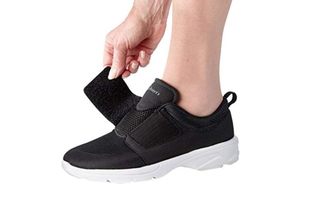 A person wearing black adaptive sneakers that have a wide velcro strap as the closure for ease of use with limited dexterity. 