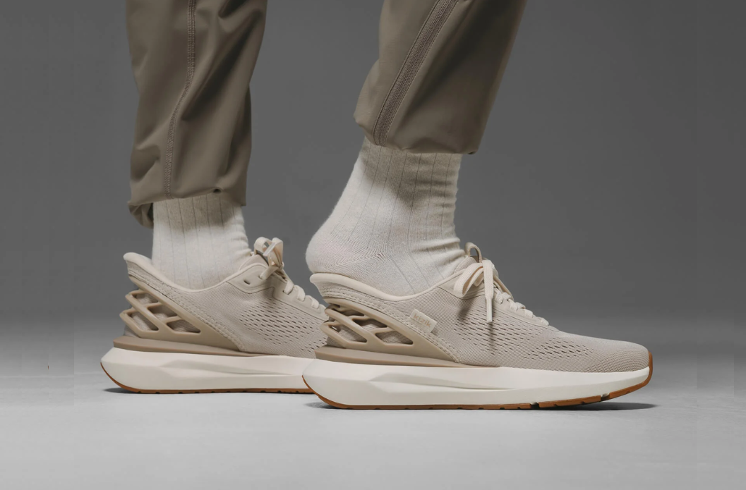 KIZIK Adaptive Slip on shoes shown in a beige tennis shoe style with white sole and cream laces. A person is stepping into the shoe with no need to bend over or use their hands.