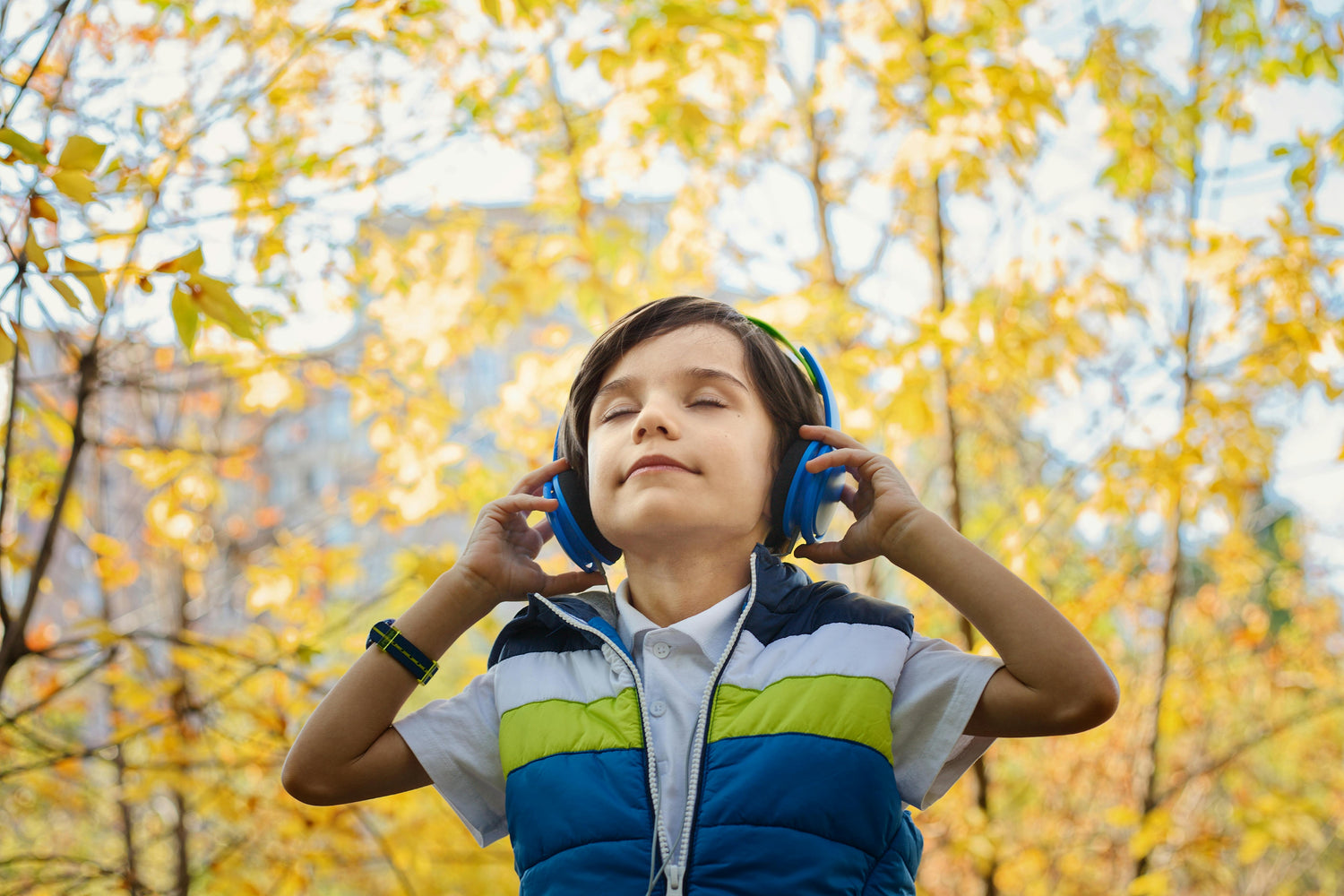 Child wearing headphones while listening attentively outdoors, surrounded by fall leaves.