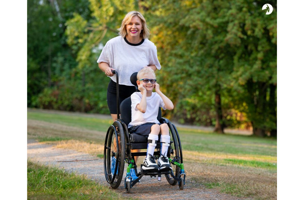 Caregiver assisting a wheelchair user with adaptive footwear during an outdoor walk.