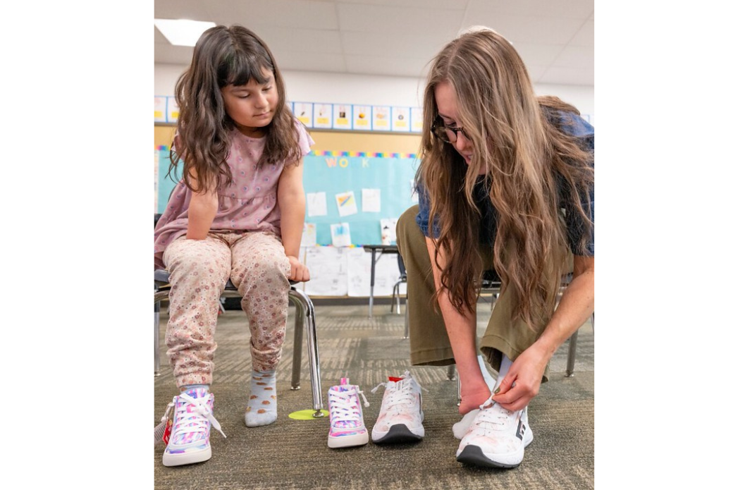 Child and adult in a classroom putting on adaptive sneakers with zipper closure for easier access.