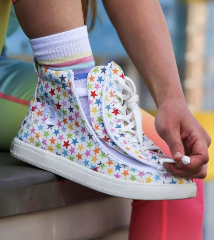 Child wearing white canvas adaptive high-top shoes with a start pattern and a wraparound zipper opening fully to fit over SMO orthotics