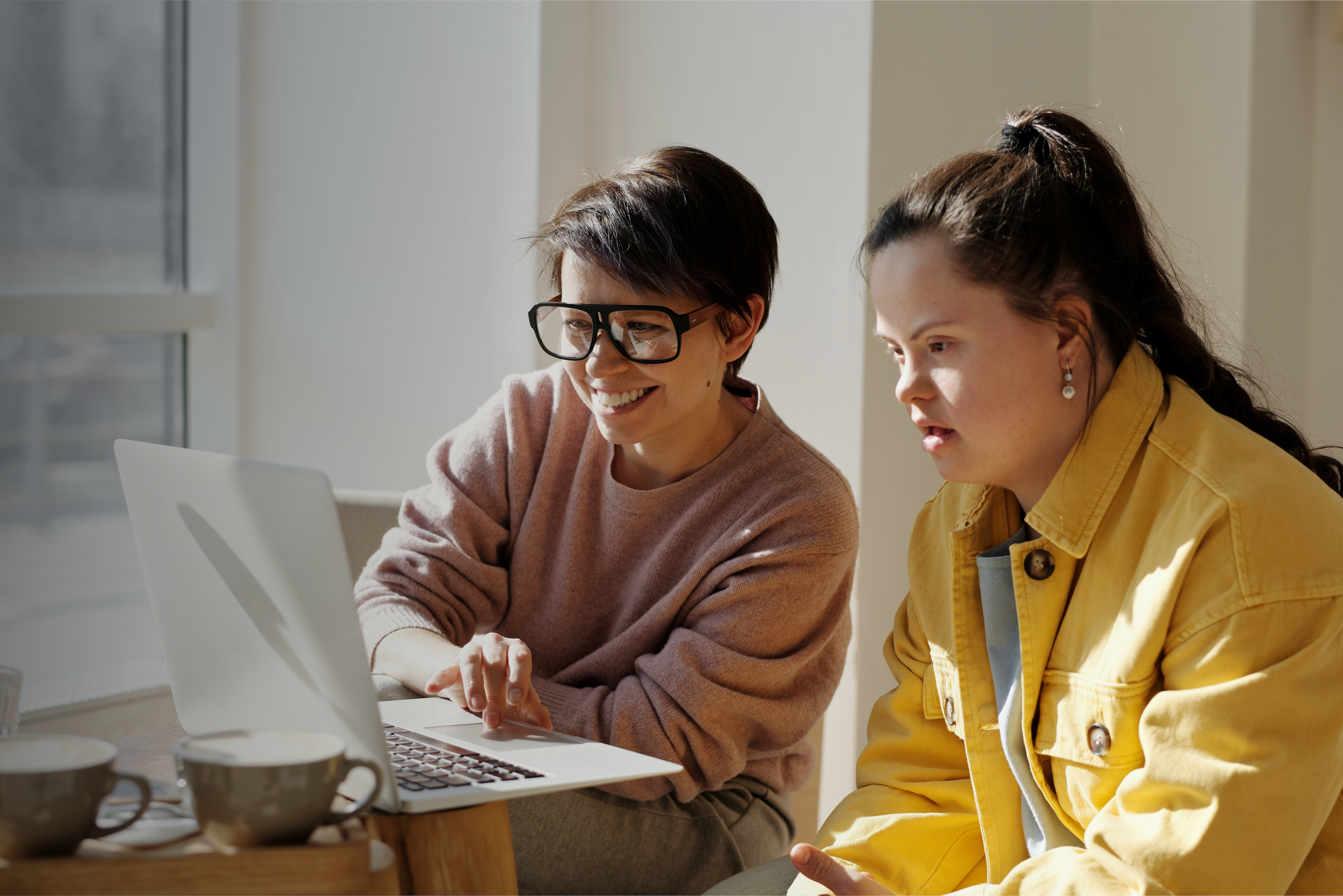 Two people sitting together reviewing something on a laptop in a bright, comfortable indoor setting.