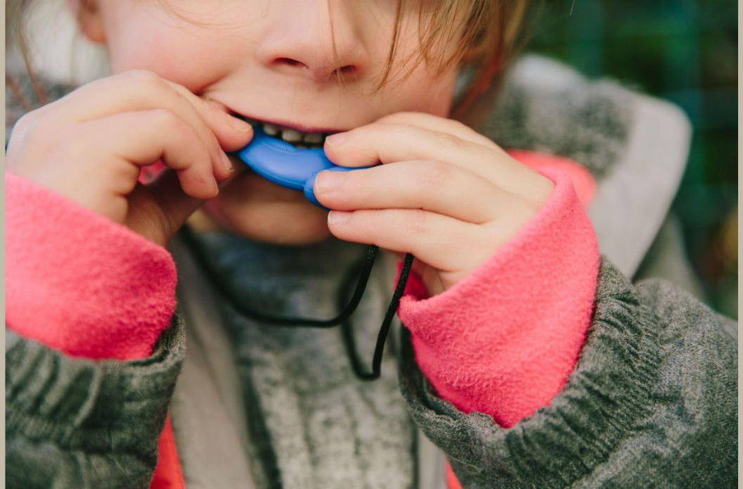 Child chewing on a blue sensory chew necklace pendant outdoors, close-up