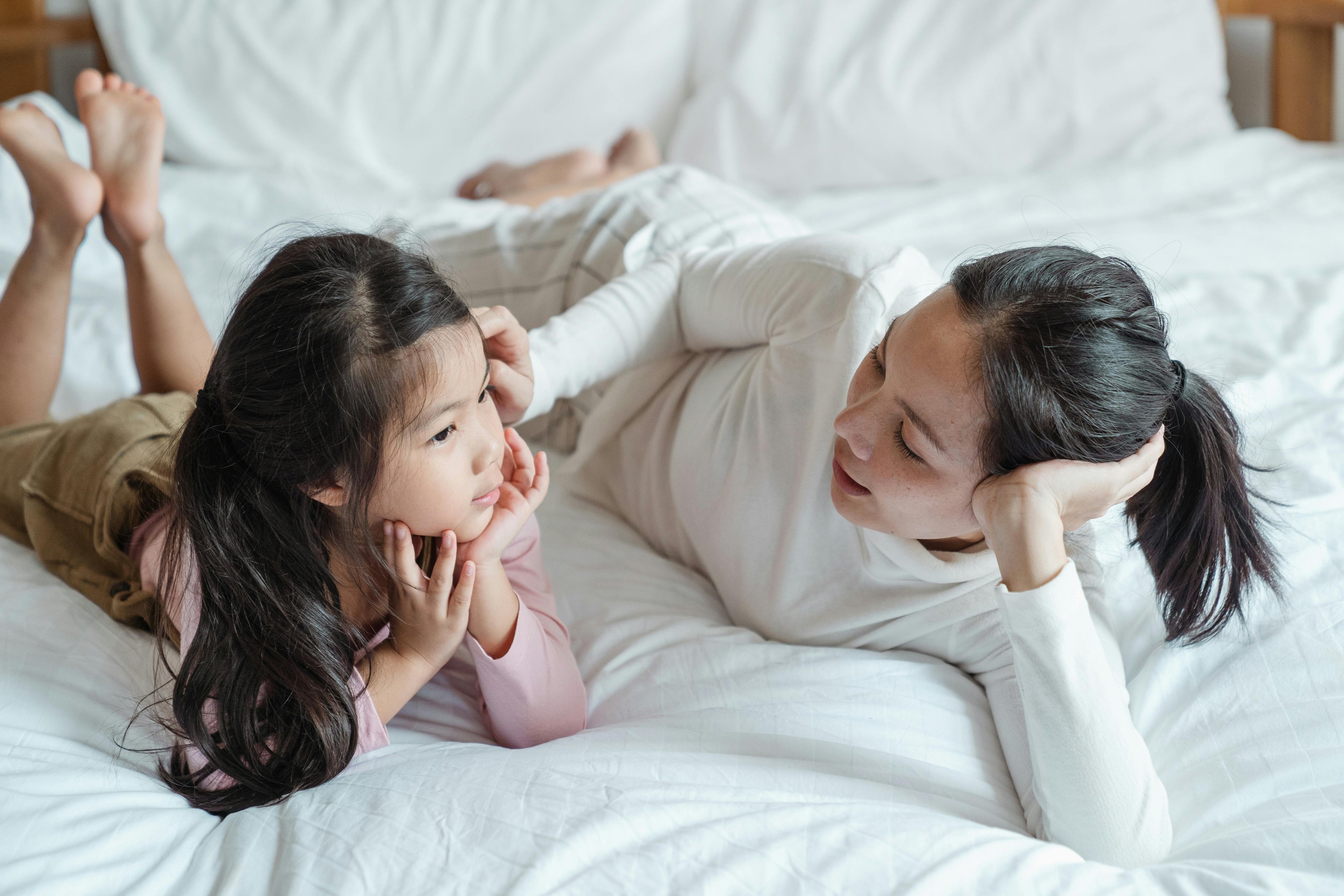 Caregiver lying on a bed talking with a young child during a quiet listening activity.