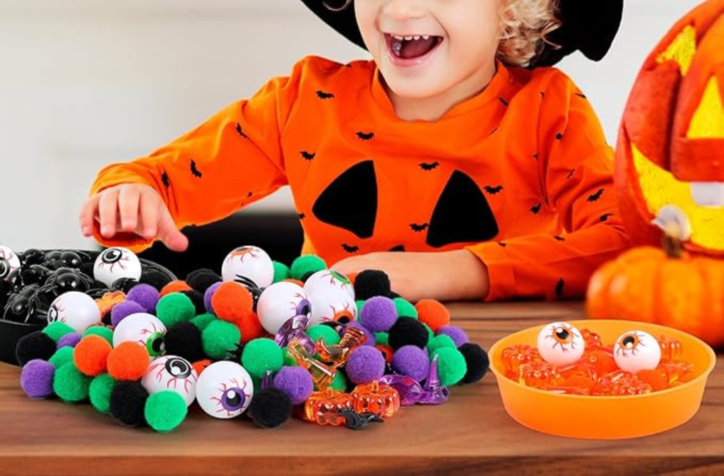 Child playing with Halloween sensory bin fillers including pom poms, toy eyeballs, and textured sensory materials