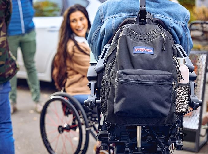 Black JanSport backpack mounted on the back of a wheelchair being worn outside with a group of friends.