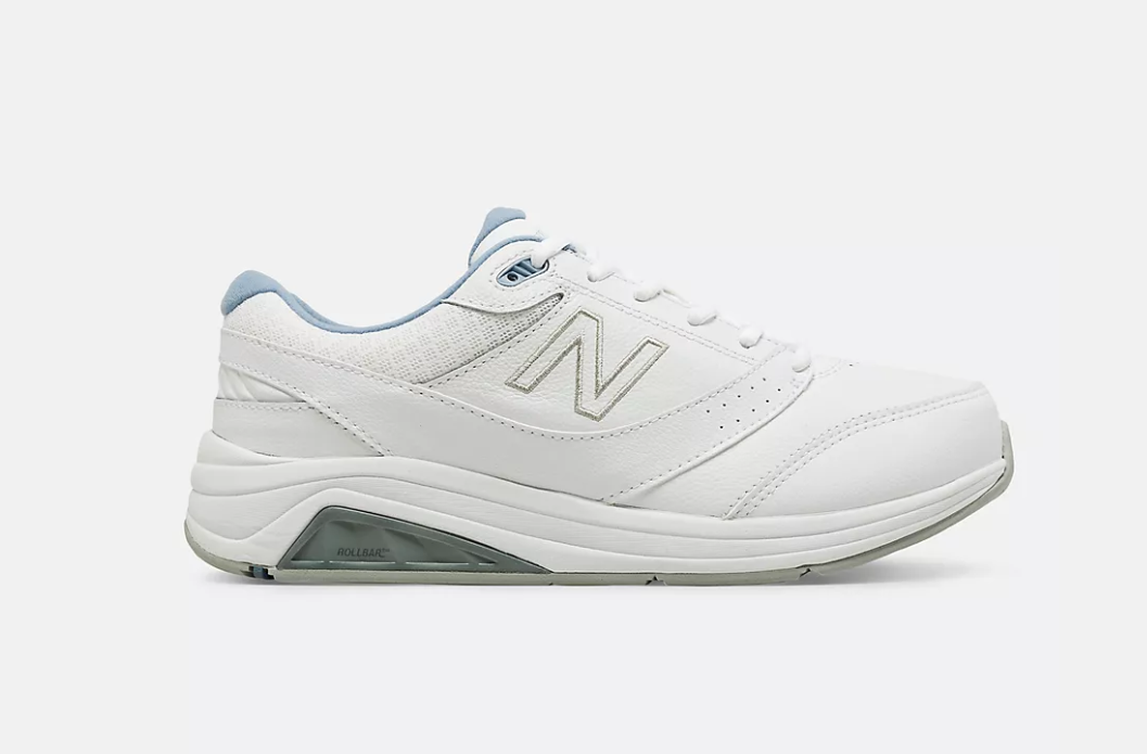 A white New Balance 928 walking shoe  with a supportive design and removable insole for adult orthotics. It has light blue accents on the collar, tongue, and heel, shown in a side profile.
