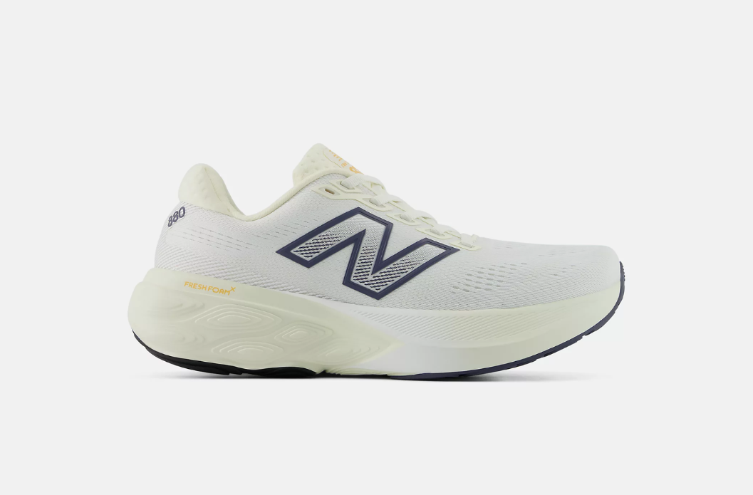 White New Balance Fresh Foam X 880 running shoe with cushioned support and multiple width options. Shown with navy and gold accents, from a side profile. 