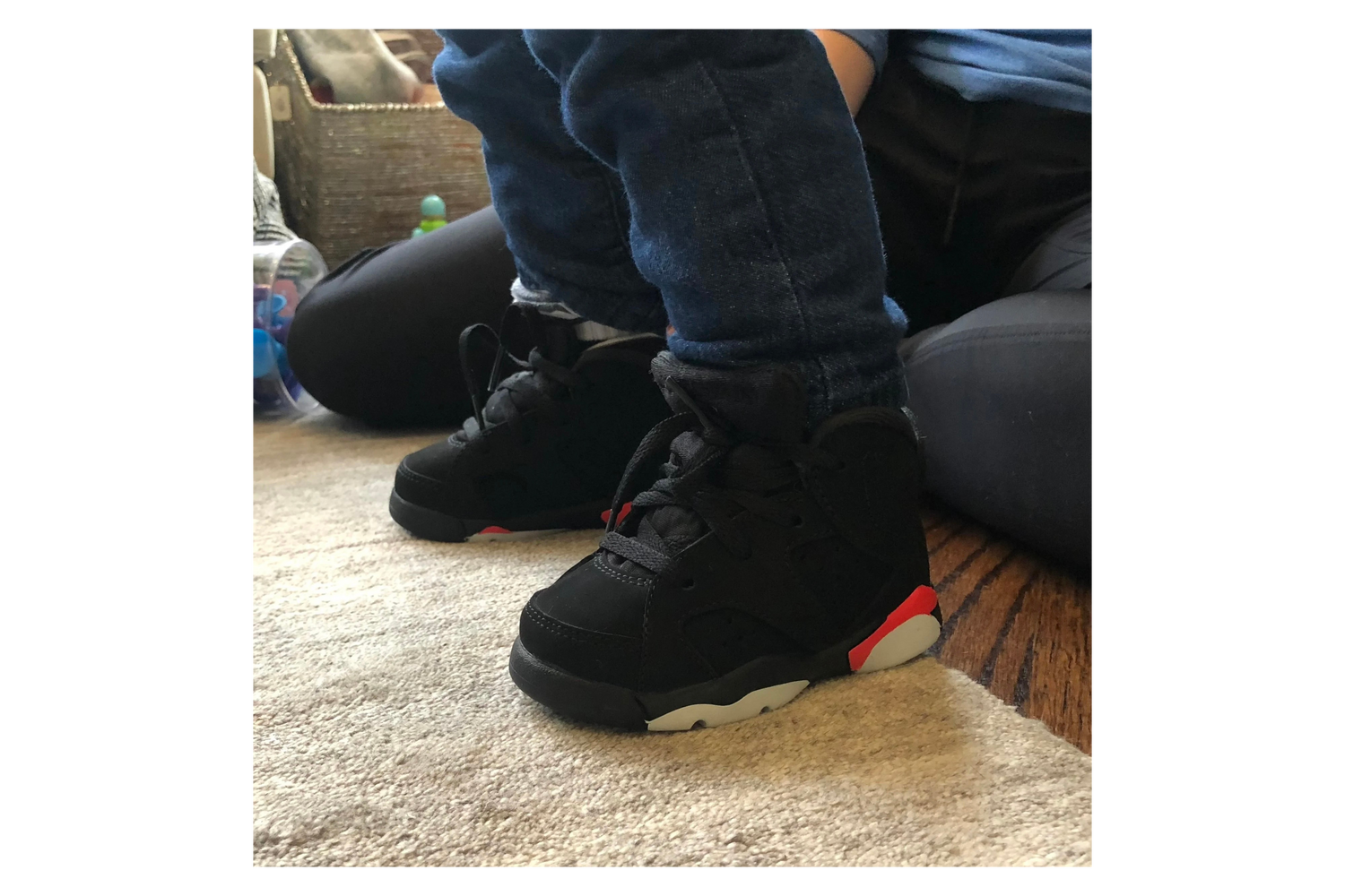Close-up of a child's feet wearing black and pink high-top Air Jordan sneakers over SMOs, indoors