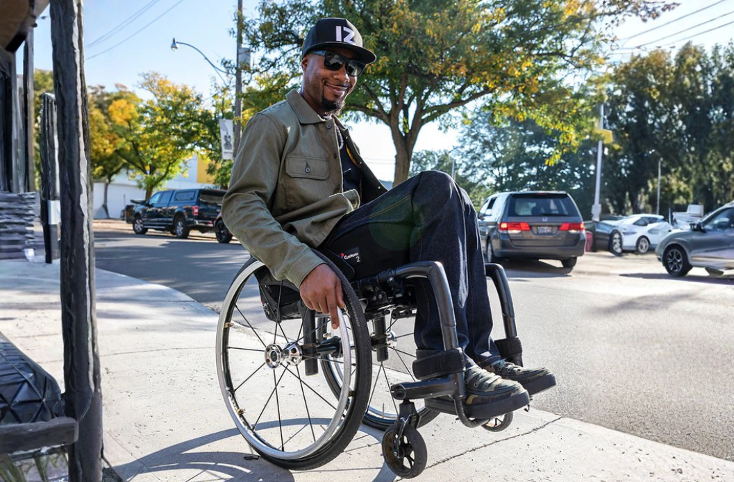 Man seated in a wheelchair outdoors wearing jacket and adaptive pants designed for comfort and mobility.