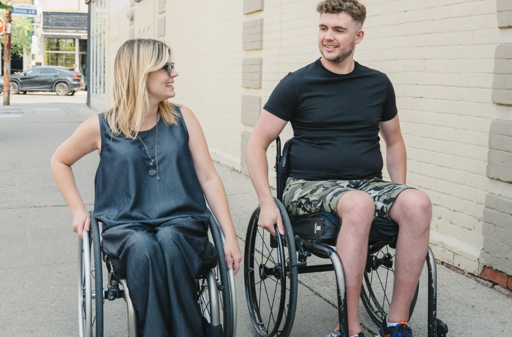 Two adults seated in wheelchairs talking while outdoors