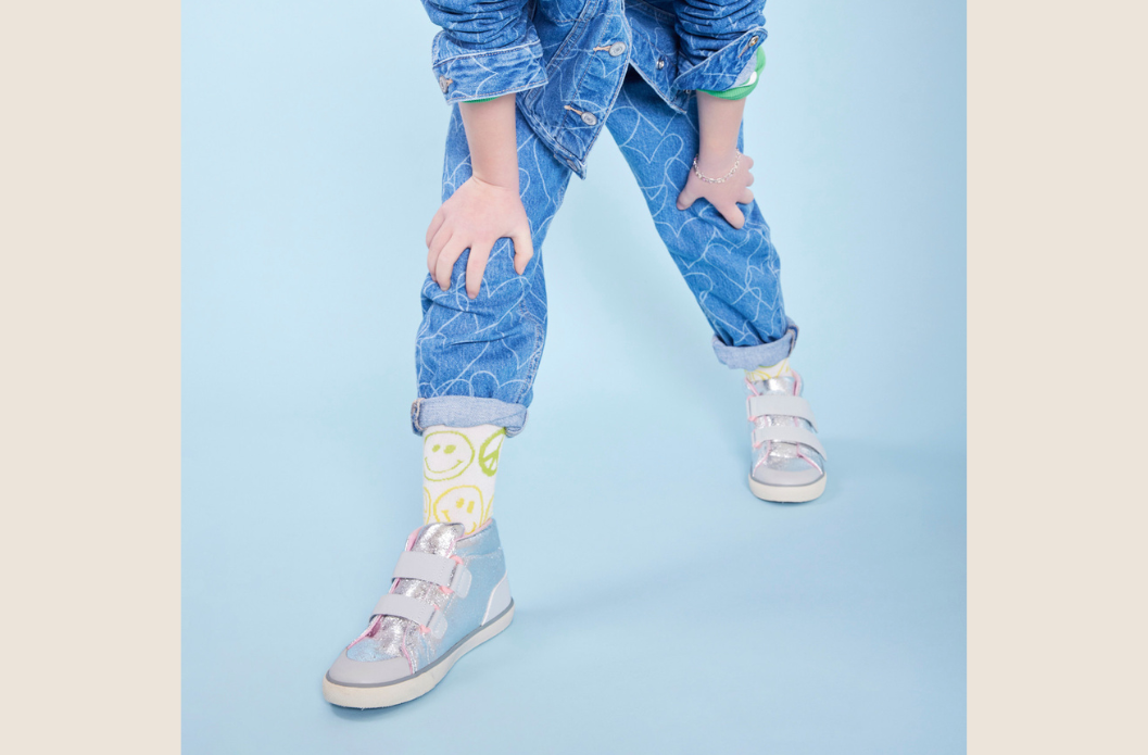Child in jeans and a denim jacket wearing smiley face socks and lightweight See Kai Run shoes designed for everyday comfort and active school days.