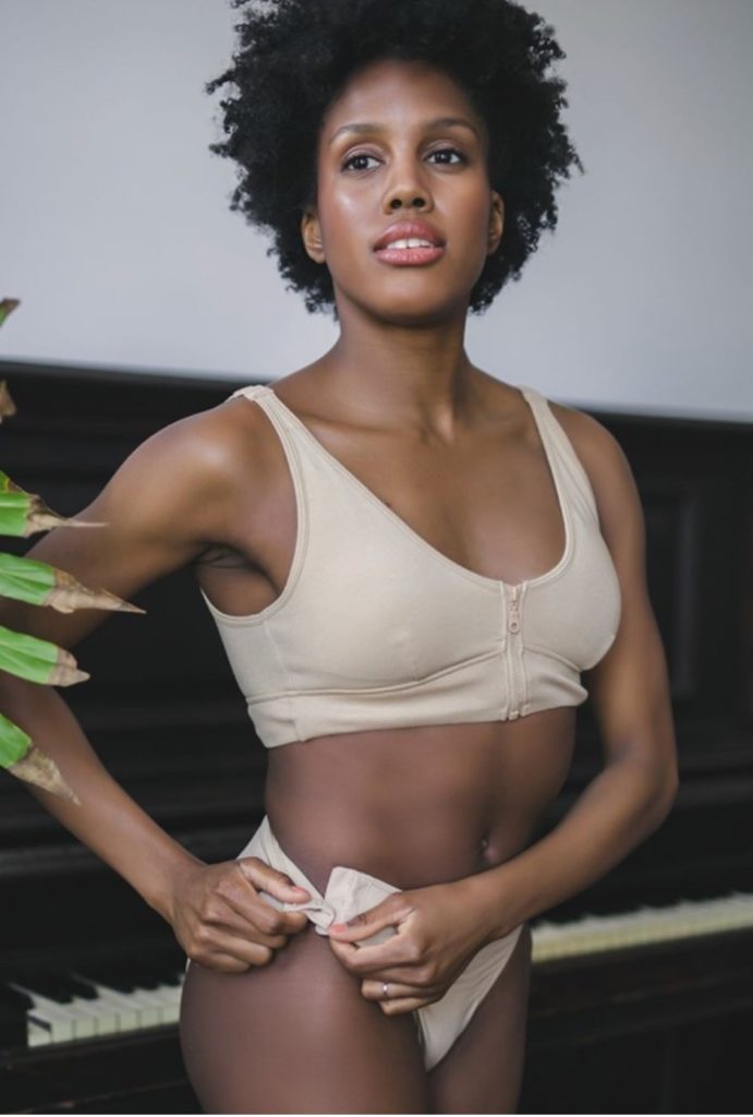 Woman wearing Slick-Chicks beige front-zip adaptive bra and adaptive underwear standing in front of a piano.