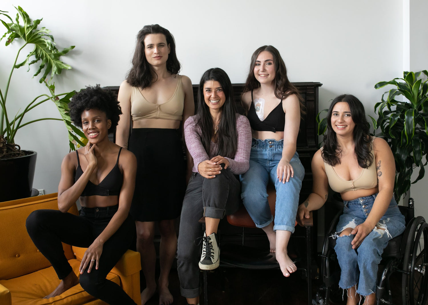 Women wearing Slick Chicks adaptive bras and apparel, including a wheelchair user, representing inclusive adaptive fashion. They are sitting at a piano and on a sofa.