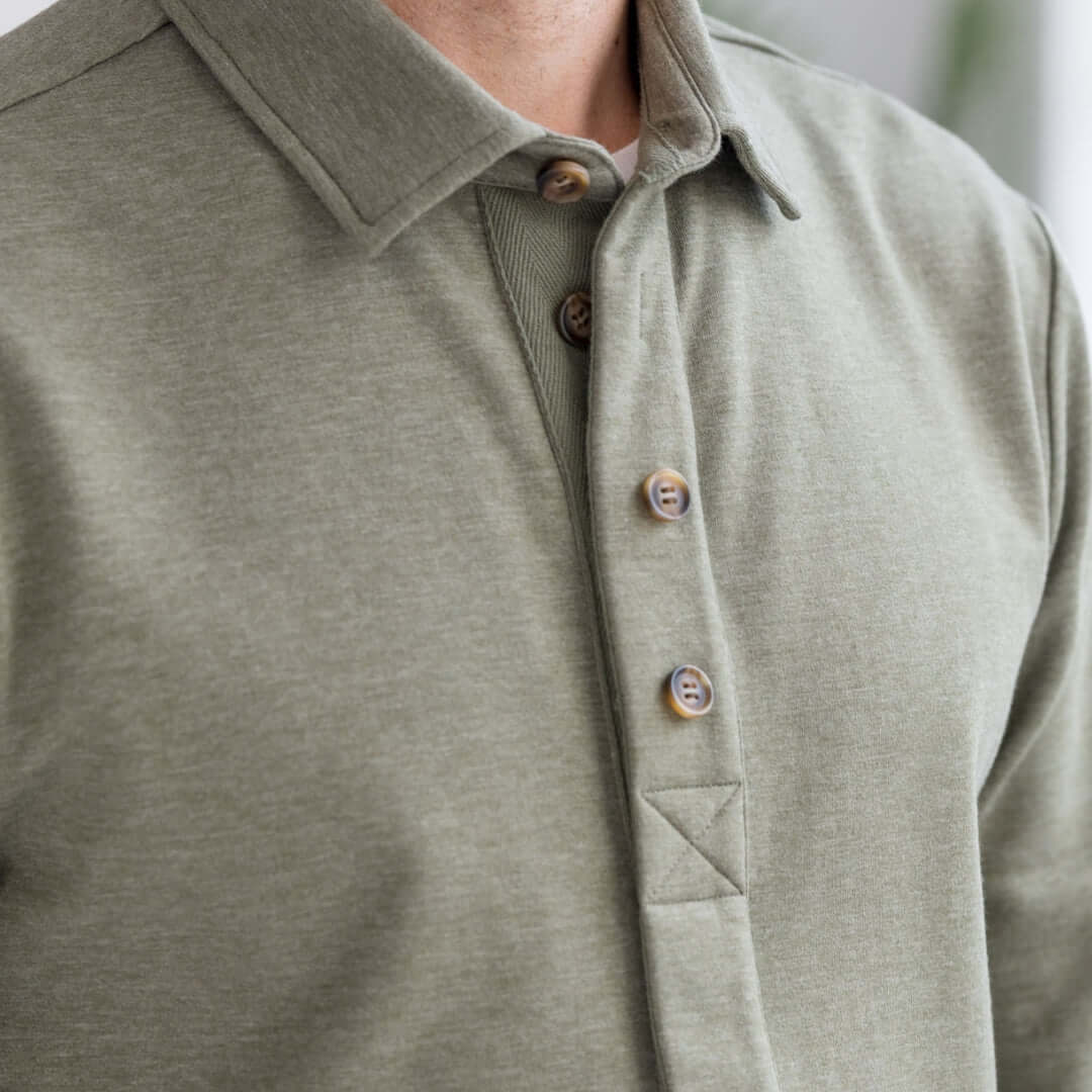 Close-up of a person wearing MagnaReady heathered olive sweatshirt, showing the magnetic front closure detail, with a blurred background.