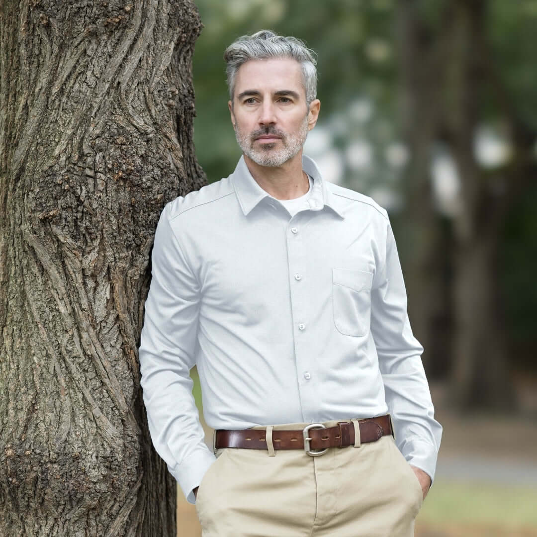 Man wearing MagnaReady white magnetic cooling shirt and khaki pants leaning against a tree in a park.