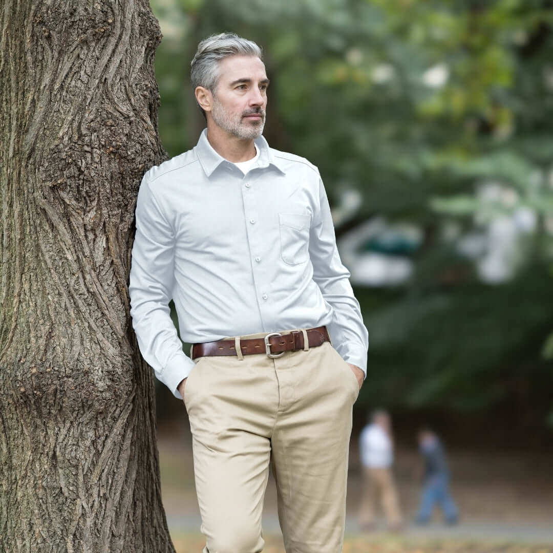 Man wearing MagnaReady white magnetic cooling shirt with khaki pants leaning against a tree in a park.