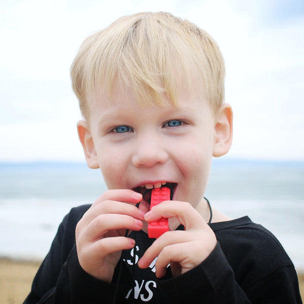 Young child chewing on a red chewelry brick necklace at the beach