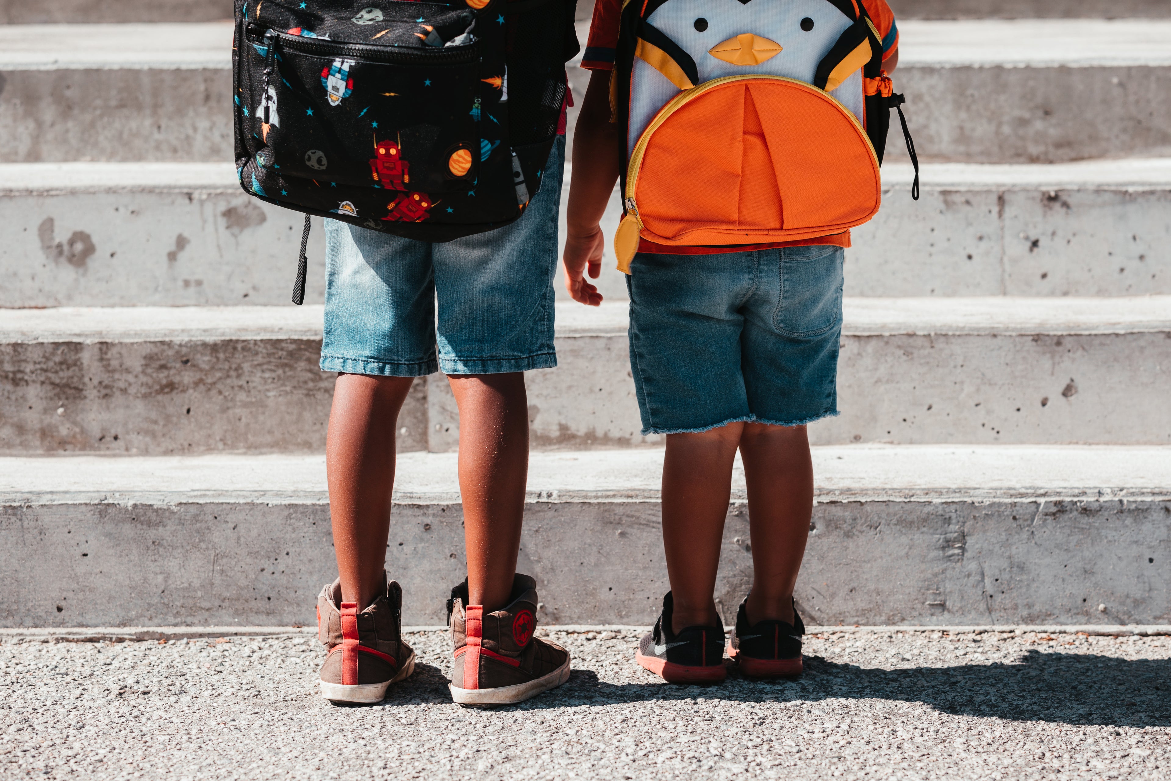 Two children wearing backpacks and school shoes while standing on school steps before class.