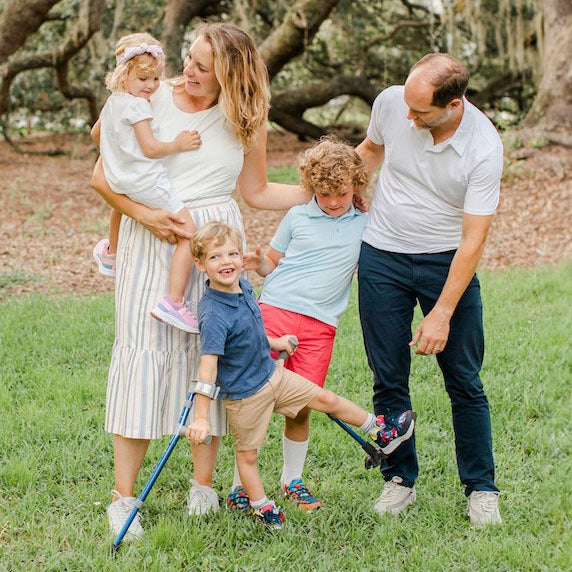 Family outdoors with children wearing adaptive shoes, including a child using forearm crutches.
