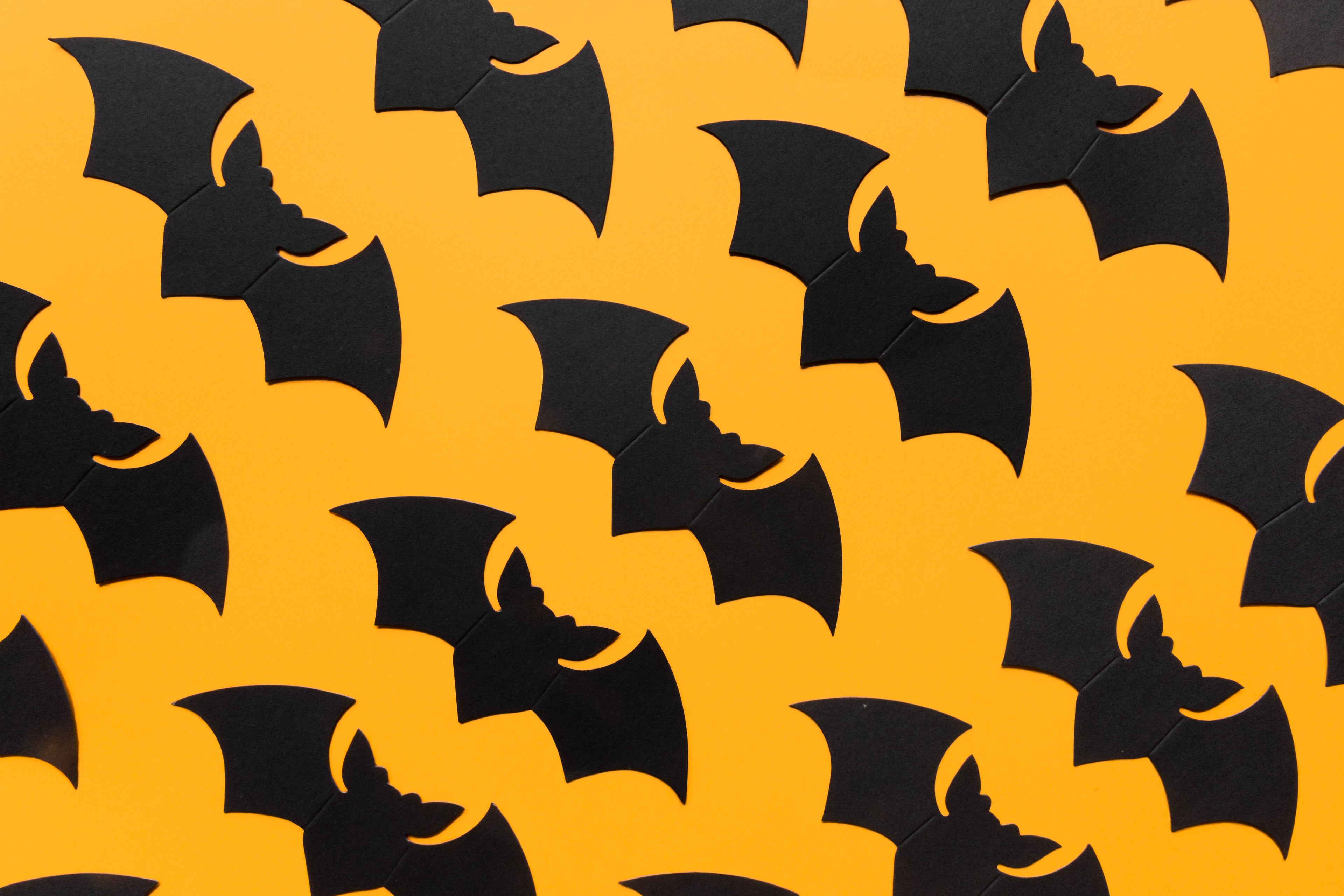 A halloween pattern with an orange background and cutout black bat shapes repeating.