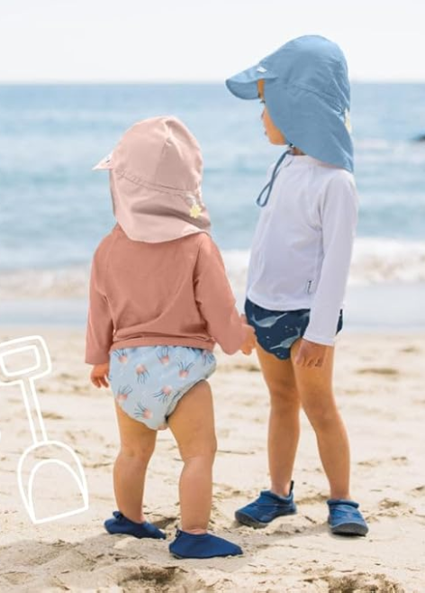 Two young children standing on the beach wearing lightweight long-sleeve rash guards and swim bottoms designed with soft, smooth fabric for comfortable movement.