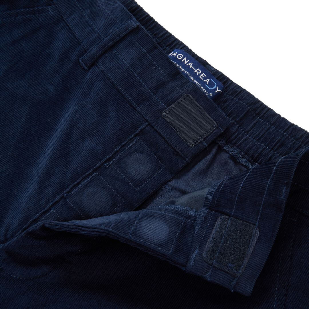 Close-up of MagnaReady navy corduroy pants magnetic fly detail with a brand label on a white background.
