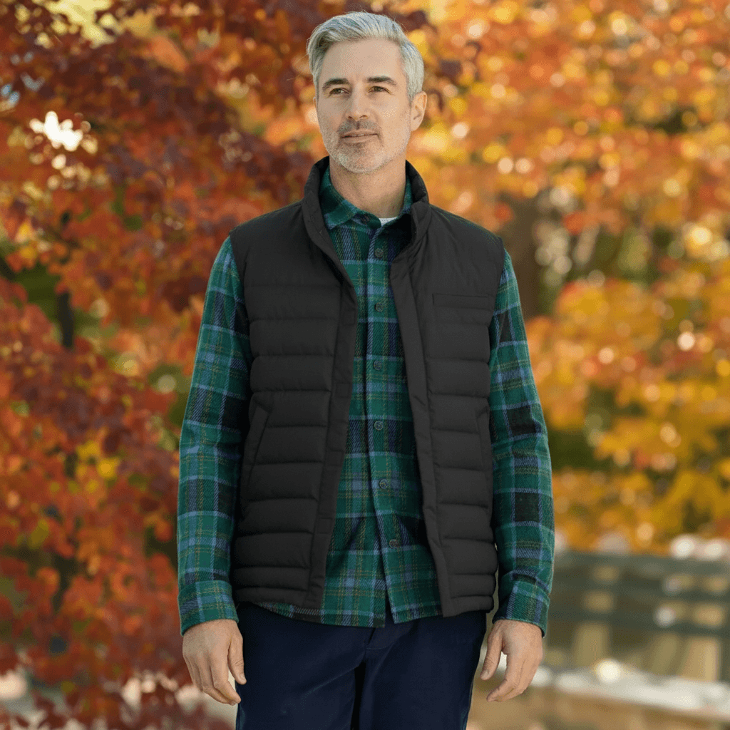 Man wearing MagnaReady black magnetic puffer vest over a plaid shirt with autumn foliage in the background.