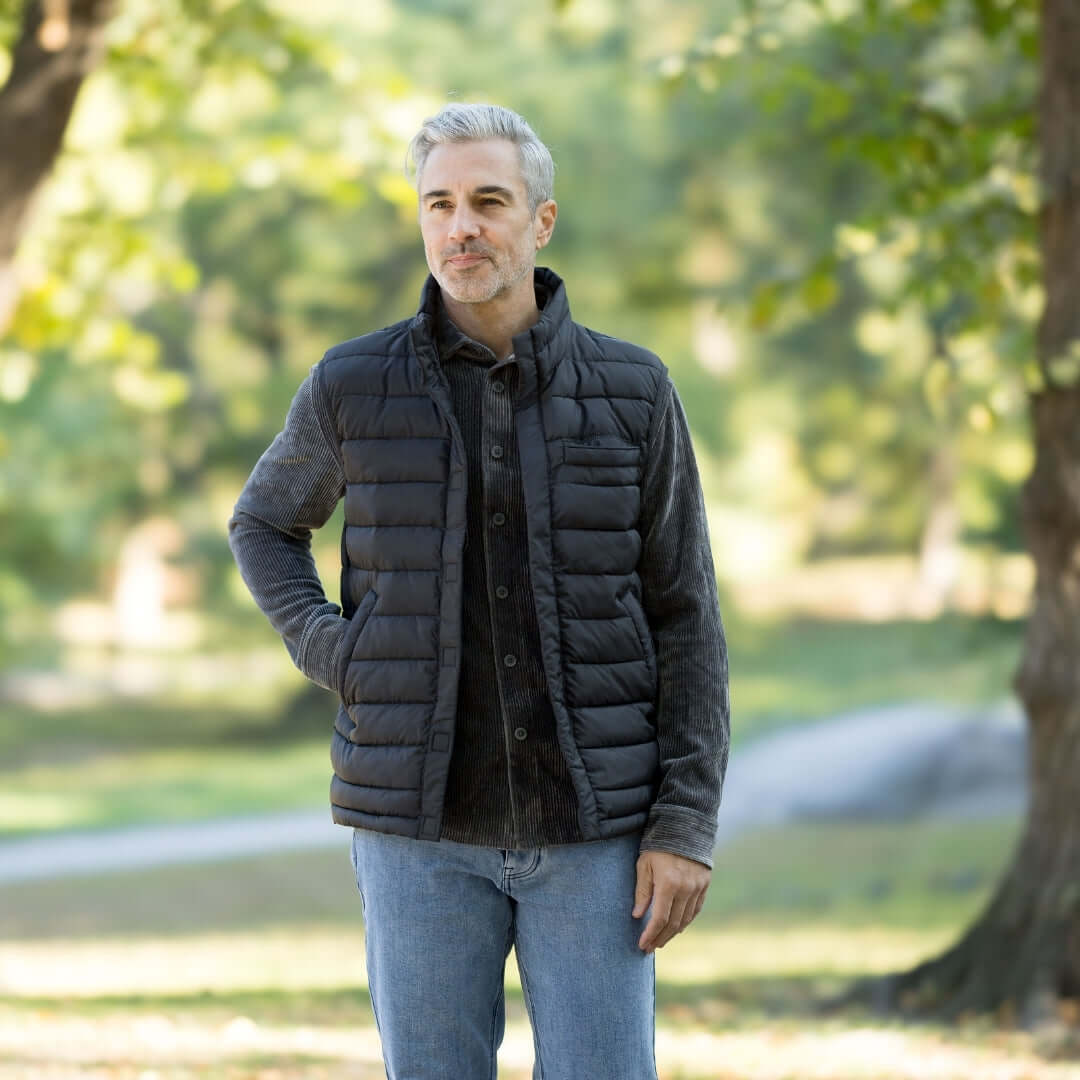 Man wearing MagnaReady black magnetic puffer vest with hands in pockets in a park setting.