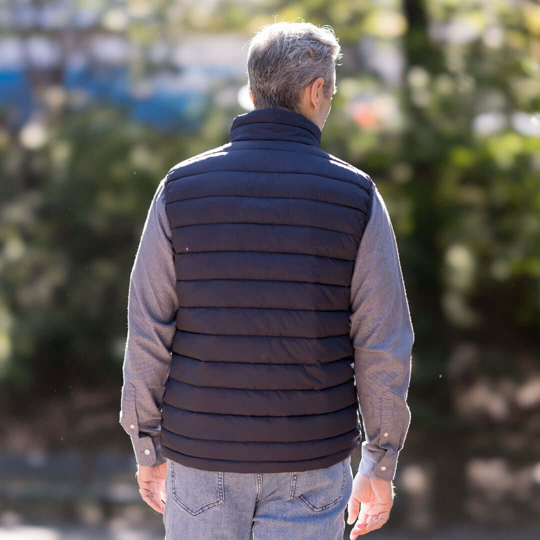 Man wearing MagnaReady black magnetic puffer vest, back view, outdoors with blurred greenery in the background.