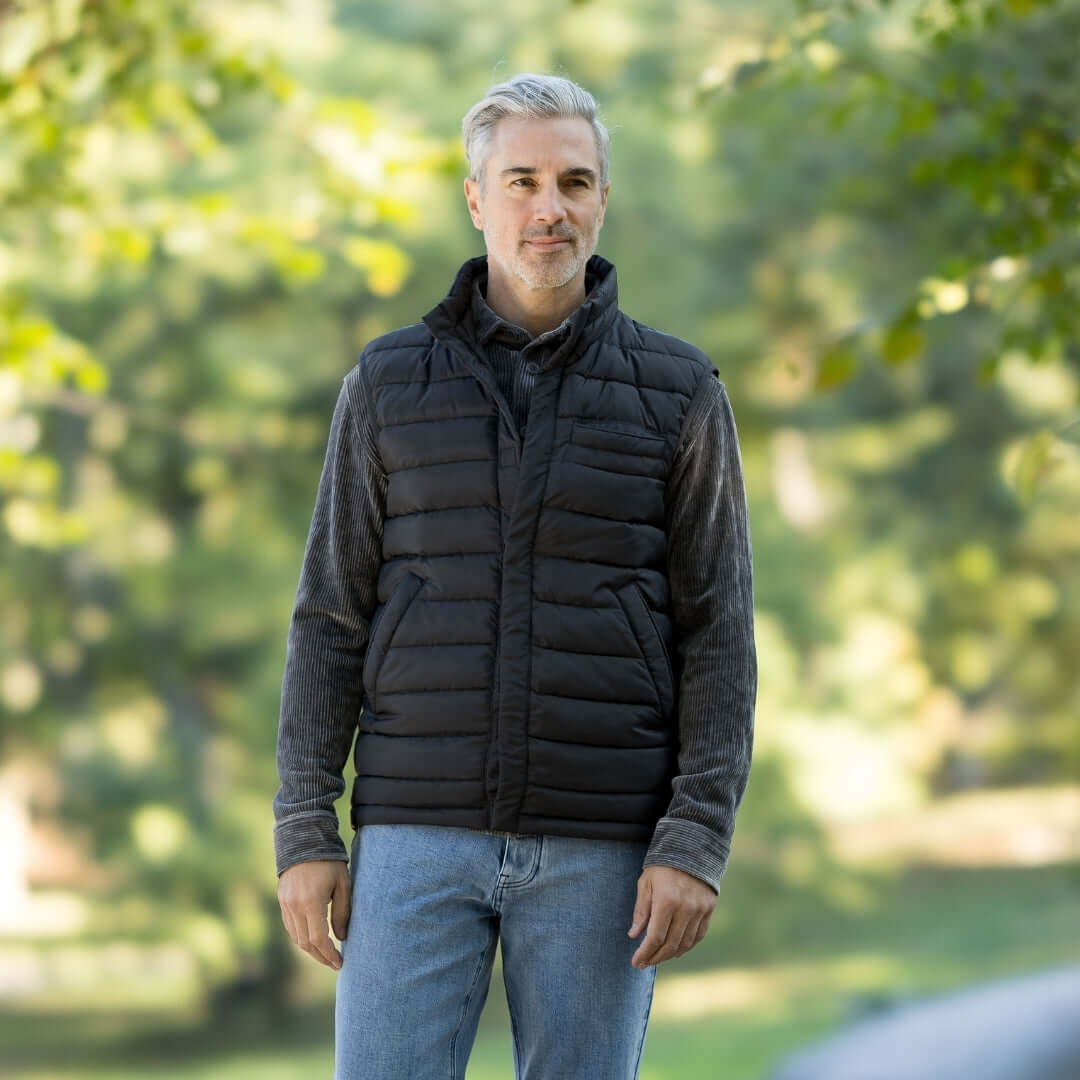 Man wearing MagnaReady black magnetic puffer vest, front view, standing outdoors with greenery in the background.
